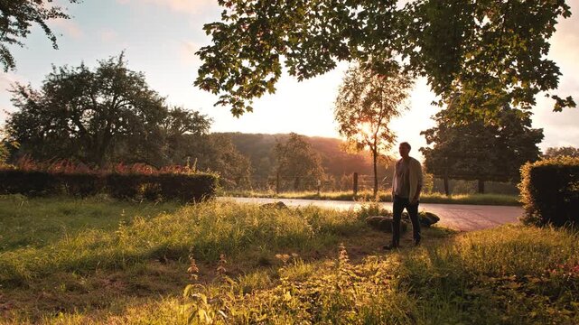 Man casually walking in a green idyll at sunset. Wide angle slow motion footage of an adult enjoying the light mood in a scenic rural paradise