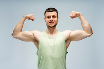 Naklejka premium Athletic man flexing muscles showing biceps triceps on grey background looking at camera