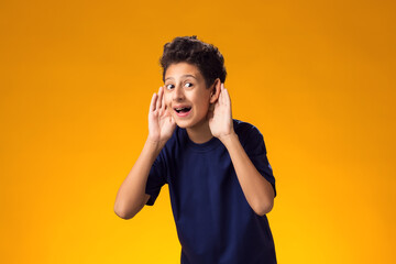 Kid boy eavesdropping, overhearing confidential secret conversation, keeping hand at his ear....
