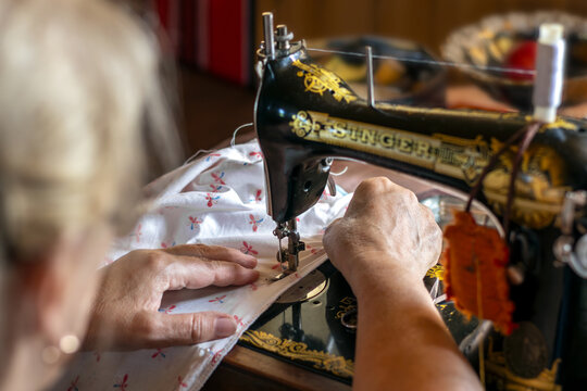 Moscow - July 01, 2024: Senior woman is sewing on an vintage sewing machine Singer. Close-up of hands