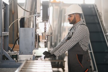 Operator of machine. Industrial worker indoors in factory. Young technician in white hard hat