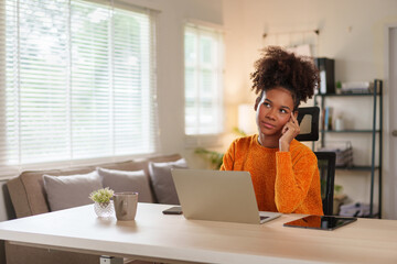 Young black woman in cozy sweater concentrating on laptop at home office during daytime.