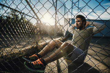 Man doing sit-ups outdoors in fenced area during sunset