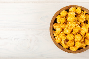 Sweet caramel popcorn in a bowl on a wooden background. Salted caramel popcorn. Caramel sauce. Close up. Topping. Place for text. Copy space