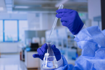 A scientist is holding a beaker filled with water and a pipette. The scene is set in a laboratory,...