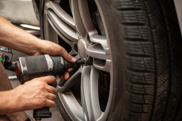 A skilled technician uses an impact wrench to fasten a wheel with a winter or summer tire on a vehicle, highlighting the precision required in seasonal tire replacement and automotive maintenance.