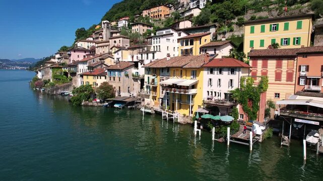 Low altitude drone view of Gandria village colorful houses on Lugano lake. Scenic Swiss traditional architecture rising from water at Italy border. Quiet lakeside street with no people, 4k video.