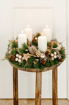 Ein eleganter Adventskranz aus Tannenzweigen, Kiefernzapfen und goldenen Akzenten auf einem rustikalen Holztisch, der mit seinen brennenden Kerzen eine gem&uuml;tliche, weihnachtliche Atmosph&auml;re schafft