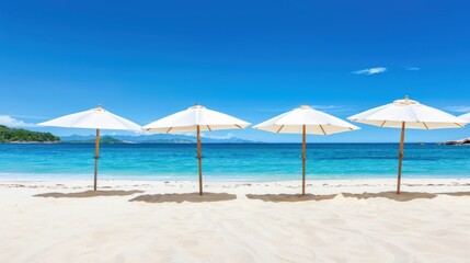 Fototapeta premium Four white beach umbrellas on a pristine sandy beach with turquoise water and a clear blue sky. Idyllic tropical vacation concept.