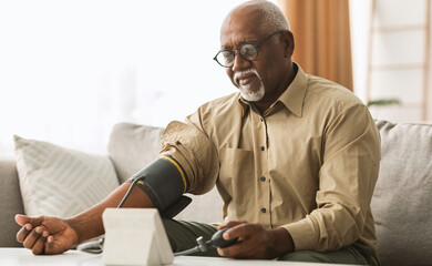 Hypertension In Older Age. Senior Black Man Measuring Arterial Blood Pressure Having Problems With Tension, Using Blood-Pressure Cuff Sitting On Sofa At Home. Healthcare And Medicine Concept