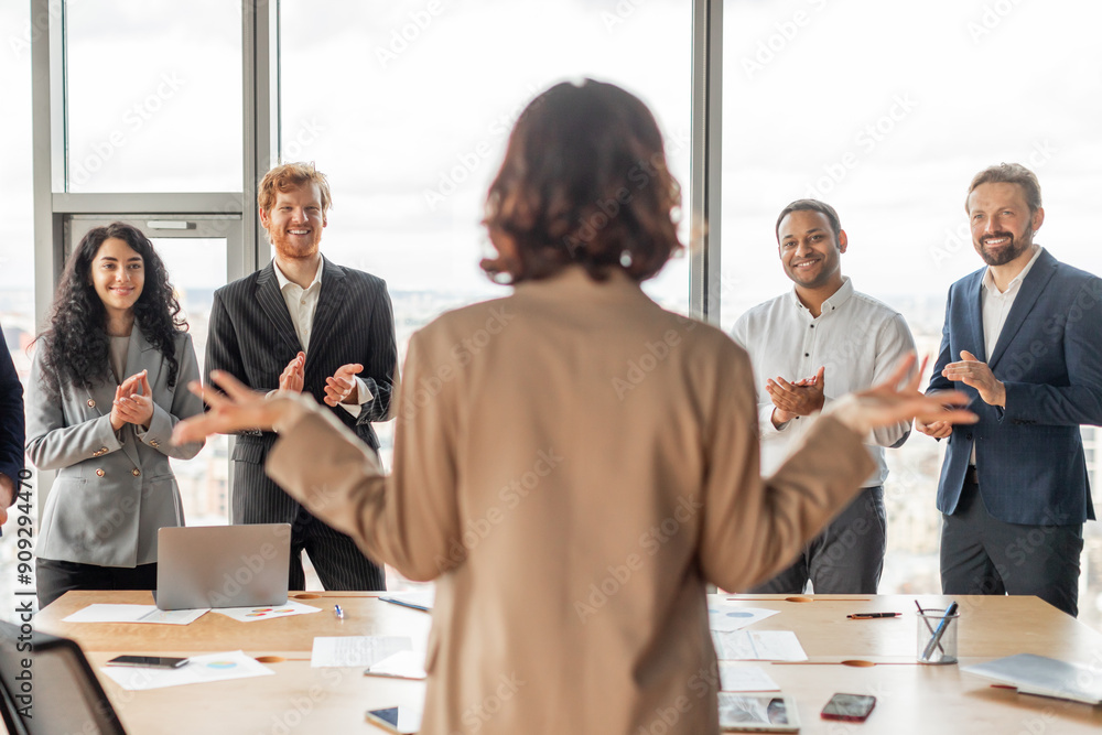 Poster a woman stands in front of a group of colleagues who are all clapping for her in a modern office set
