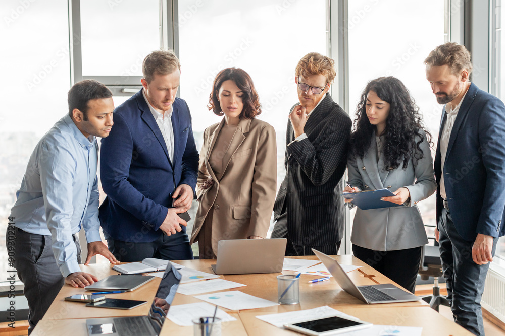 Fototapete a group of diverse business professionals in formal attire gather around a table in a modern office 
