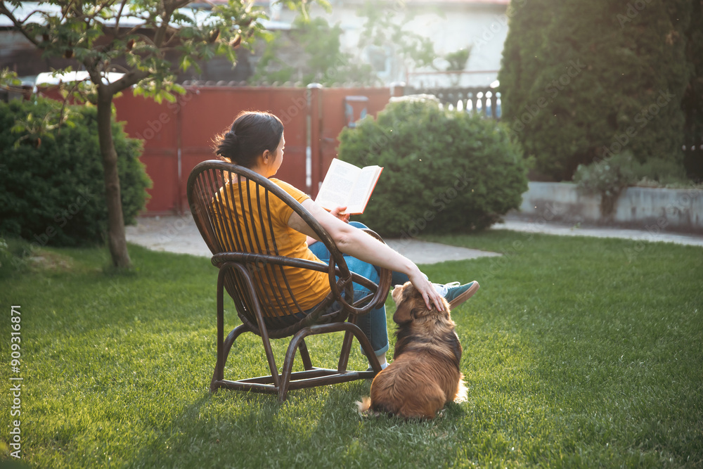 Wall mural woman reading a book in her garden with her dog