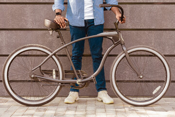 Unrecognizable Afro Man Holding Bicycle With Stylish Design, Standing Over Grey Urban Wall, Cropped Image, Closeup
