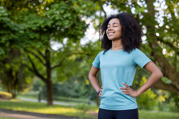Confident young African American athlete smiling with hands on hips in park. Feeling of achievement...