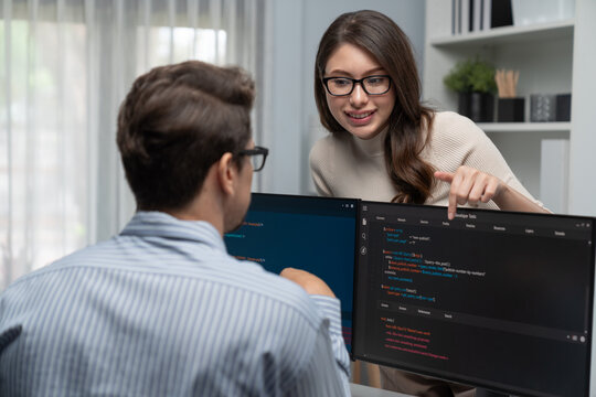 Woman colleague standing opposite to man programmer working on desk to discuss coding website software system project on two pc screen, comparing with typing full stack data prompt design. Postulate.