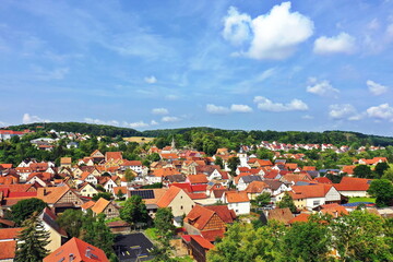 Ein Luftbild von Maßbach mit Blick auf eine malerische Stadtansicht mit zahlreichen roten Dächern, die dicht beieinander liegen. Zwischen den Häusern sind grüne Flächen zu sehen.