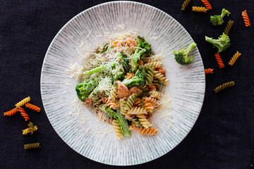 Fusilli pasta in creamy sauce with salmon and broccoli. Tricolor pasta in a white plate on a black background.