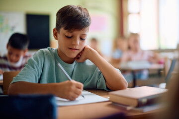 Elementary student writing in notebook during  class at school.