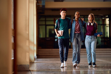 Multiracial group of happy high school students walking through hallway.