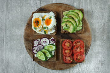 Various sandwiches on a wooden board made of black rye whole grain bread with tomato, avocado, egg and cucumber. Top view
