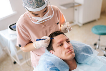 Top view of female trichologist doctor marking hair line to male patient with hairloss problem,...