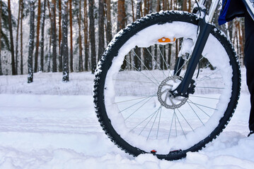 Bicycle wheel in snow on winter road in forest. Winter bicycle ride.