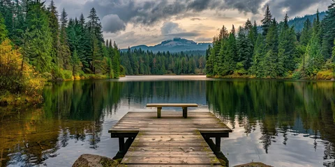 Foto op Plexiglas A lake surrounded by dense pine forests, with an old wooden dock leading to the water's edge and a bench placed on it for contemplation © GaMe
