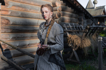 a young girl with a long blond braid in a folk costume, in a village among wooden architecture, Slavic or Nordic style