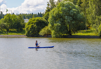 A young guy sitting down rides a SUP board, overcoming the waves with ease