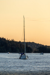 A sailboat approaching the camera on water with the sun setting behind.