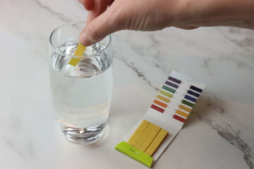Woman doing the pH test with strips in a liquid glass and showing to the camera 