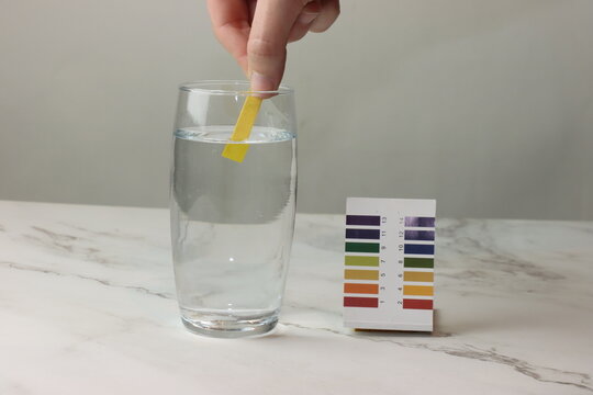 Woman doing the pH test with strips in a liquid glass and showing to the camera 