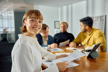 Fototapeta premium Four young multiracial adults in businesswear meeting at conference table with digital tablet in office