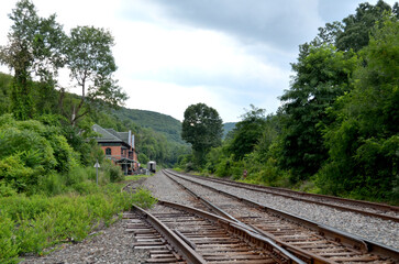 Old railroad station off the side of three railroad tracks surrounded by trees