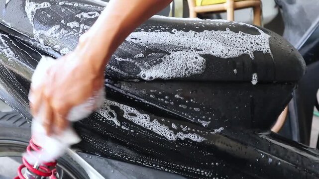 A man washing a motorbike. Mengelap sepeda motor dengan kain berbusa. 