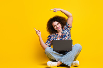 Full body photo of attractive young woman sit floor netbook point empty space dressed colorful...