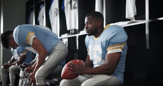 Serious men, football players and team captain with ball in locker room for match, game plan or half time. Young people or group of sports athletes in break, row or line for tournament or competition