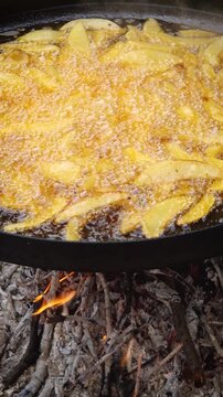 Cooking potatoes on fire outdoors. Big campfire pan with boiling oil under flame, and delicious flavour steam