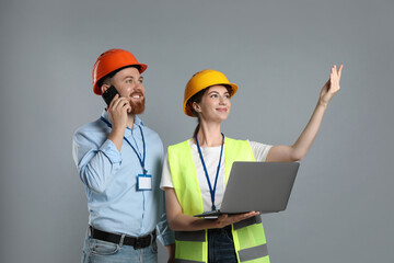 Engineer talking on smartphone while his colleague holding laptop against grey background