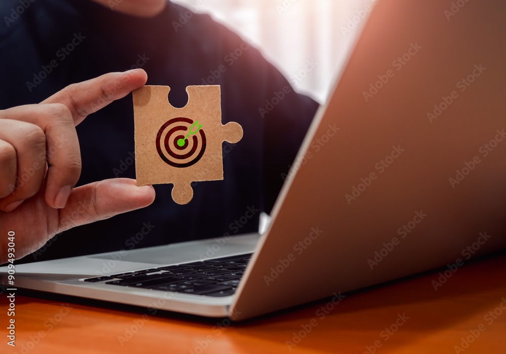 Poster green target dartboard icon on jigsaw puzzle piece holding by businessman's hand while working with 