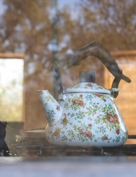 Vintage floral kettle steaming on outdoor stove, rustic morning scene