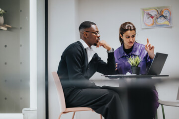 African American man and Indian woman discuss work, engrossed in a collaborative effort in a bright, contemporary office space.