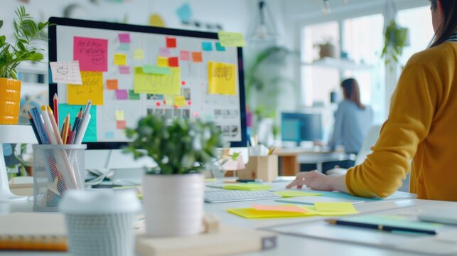 A modern office workspace featuring a computer monitor with colorful sticky notes, potted plants, pencils, and a coffee cup..