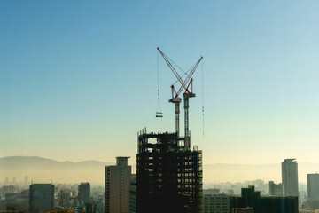 Fototapeta premium Construction site with cranes on the top of high buildings. Construction workers are building, the morning day in Osaka, Japan. Aerial view.Top view.