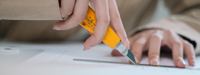 The teenage woman, working as a designer, deftly uses a cutter in her craft, meticulously drafting...