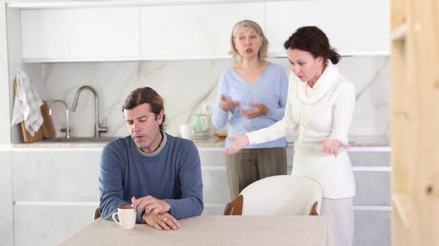 Elderly mother and woman scold swear at man. Male is upset because of family conflict, dejectedly listens to his wife and mother scolding him. Complex intergenerational relationships