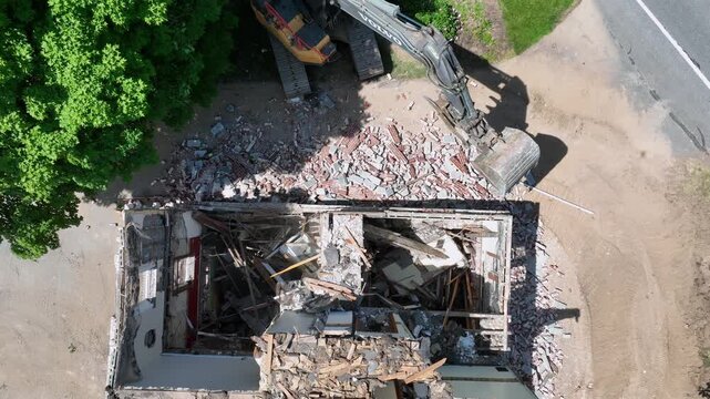 Excavator demolishing house. Ground level demolition with debris falling. Aerial of condemned home being torn down. Drone top down shot.