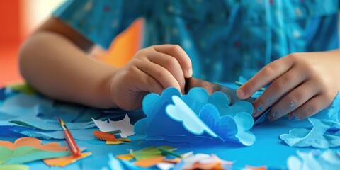 Fototapeta premium Child cutting a cloud shape from blue paper Nature themed collage art lesson in kindergarten
