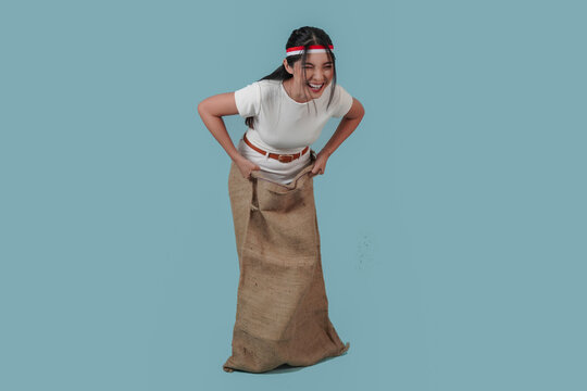 Excited Indonesian woman wearing gunny sack and jumping, joining competition.
